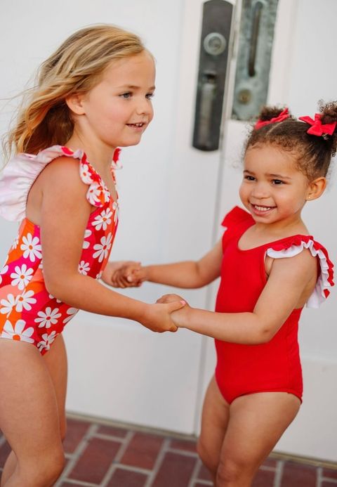 Two little girls playing, one wearing a red bathing suit and the other wearing retro daisy suit.