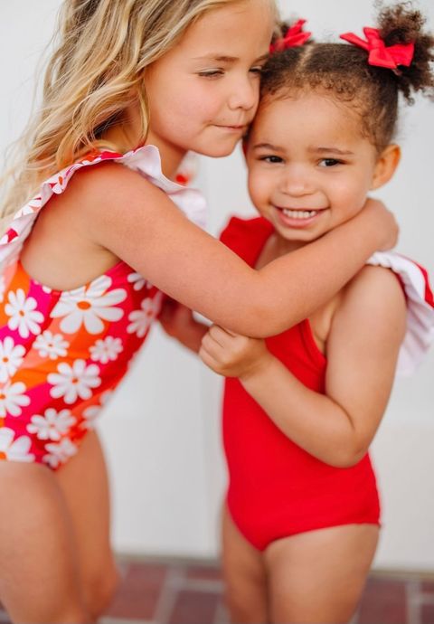 Two little girls hugging, one wearing a red bathing suit and the other wearing retro daisy suit. 